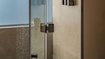 A modern shower with a rain showerhead, a glass door, and a wall-mounted faucet.