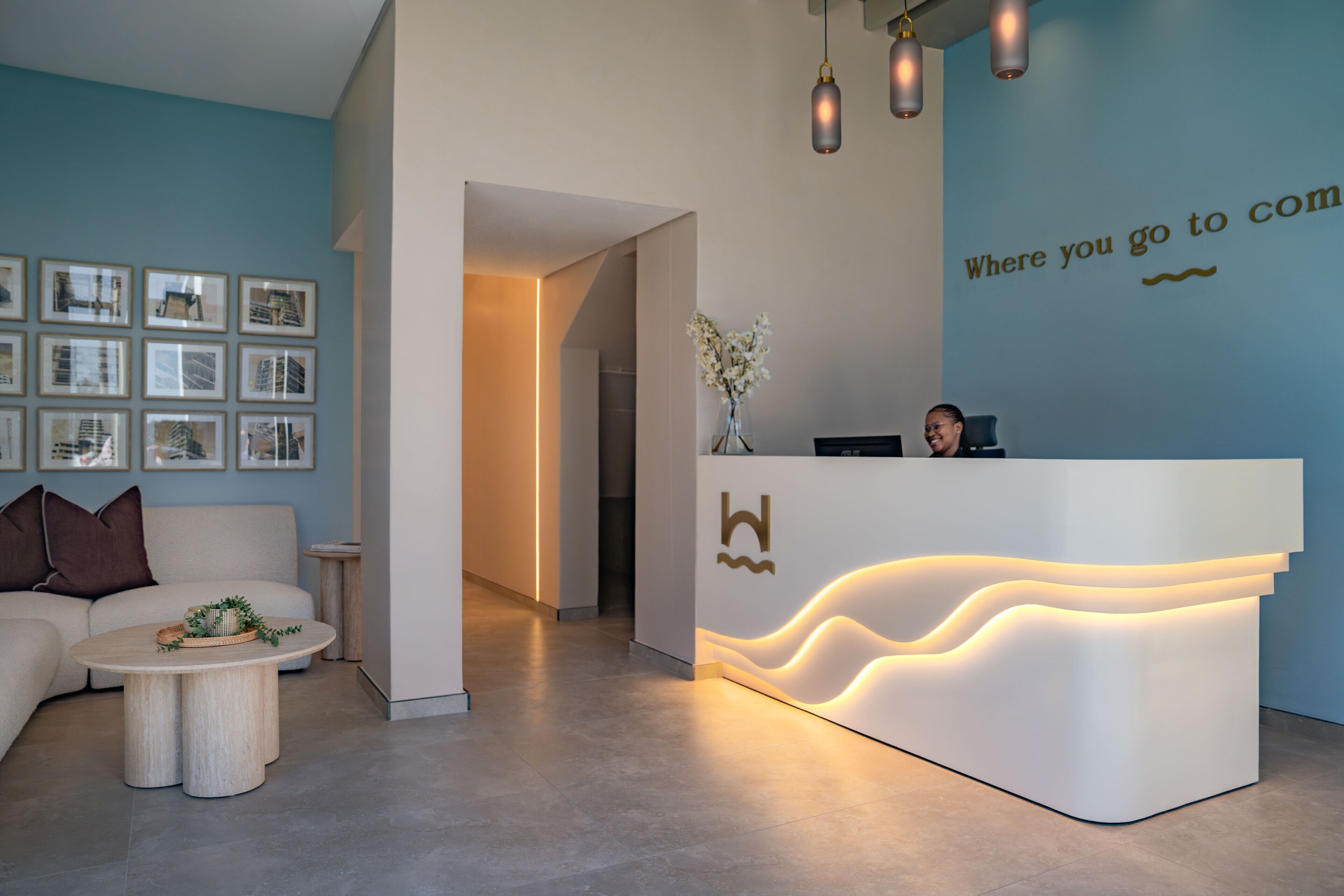 A reception desk with a modern design, framed pictures on the wall, a sofa, and a small table with a plant.