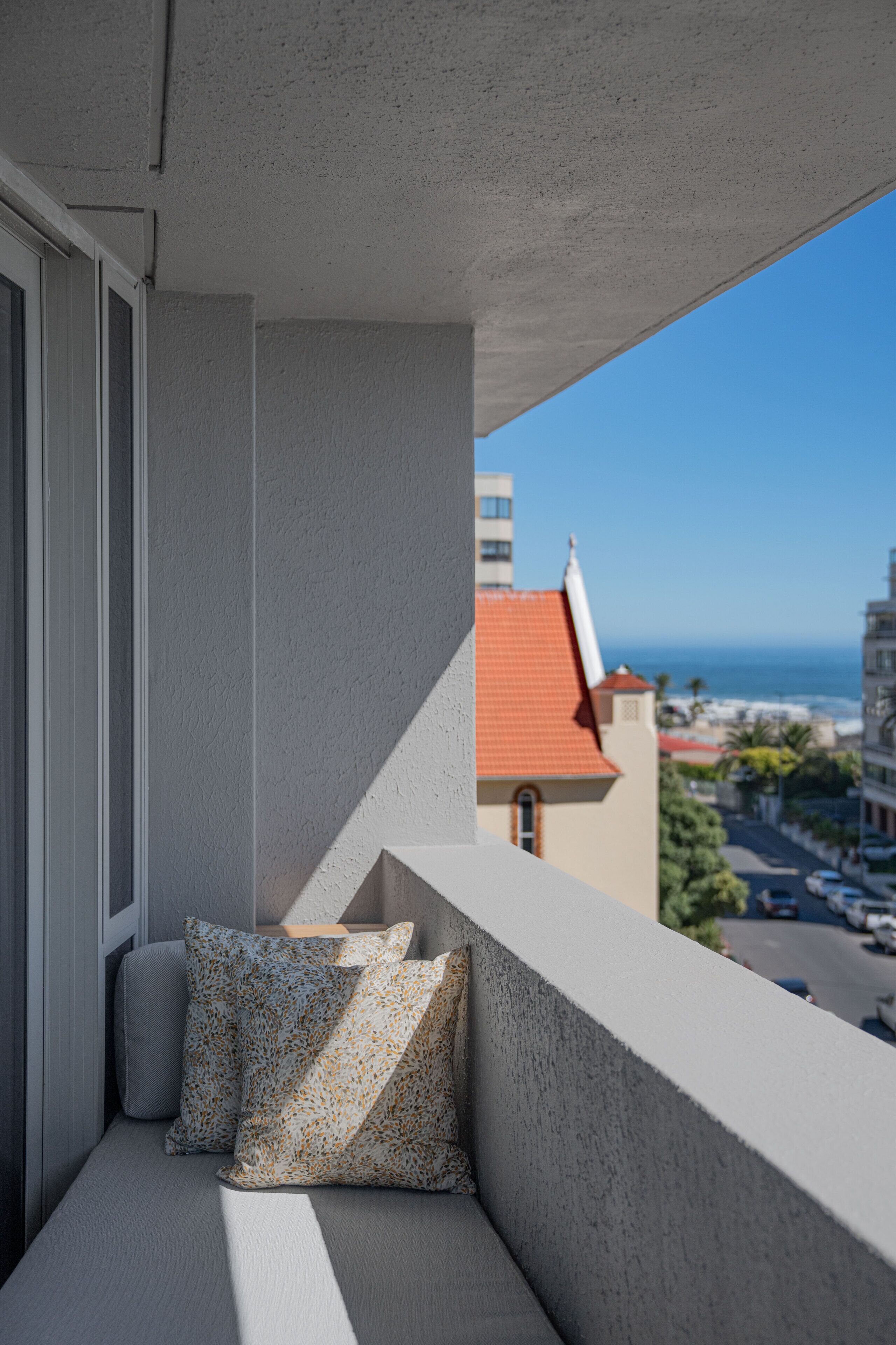 Un balcón con vista al océano y un edificio con techo rojo.