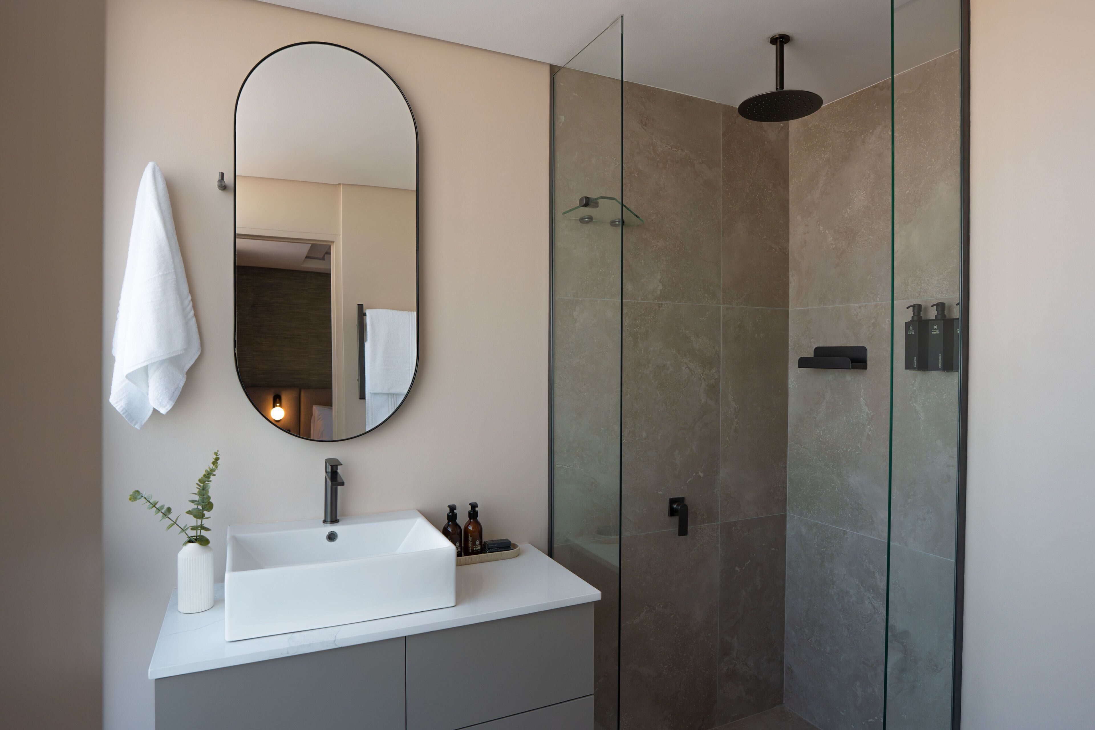 A modern bathroom with a white sink, a round mirror, and a glass-enclosed shower.