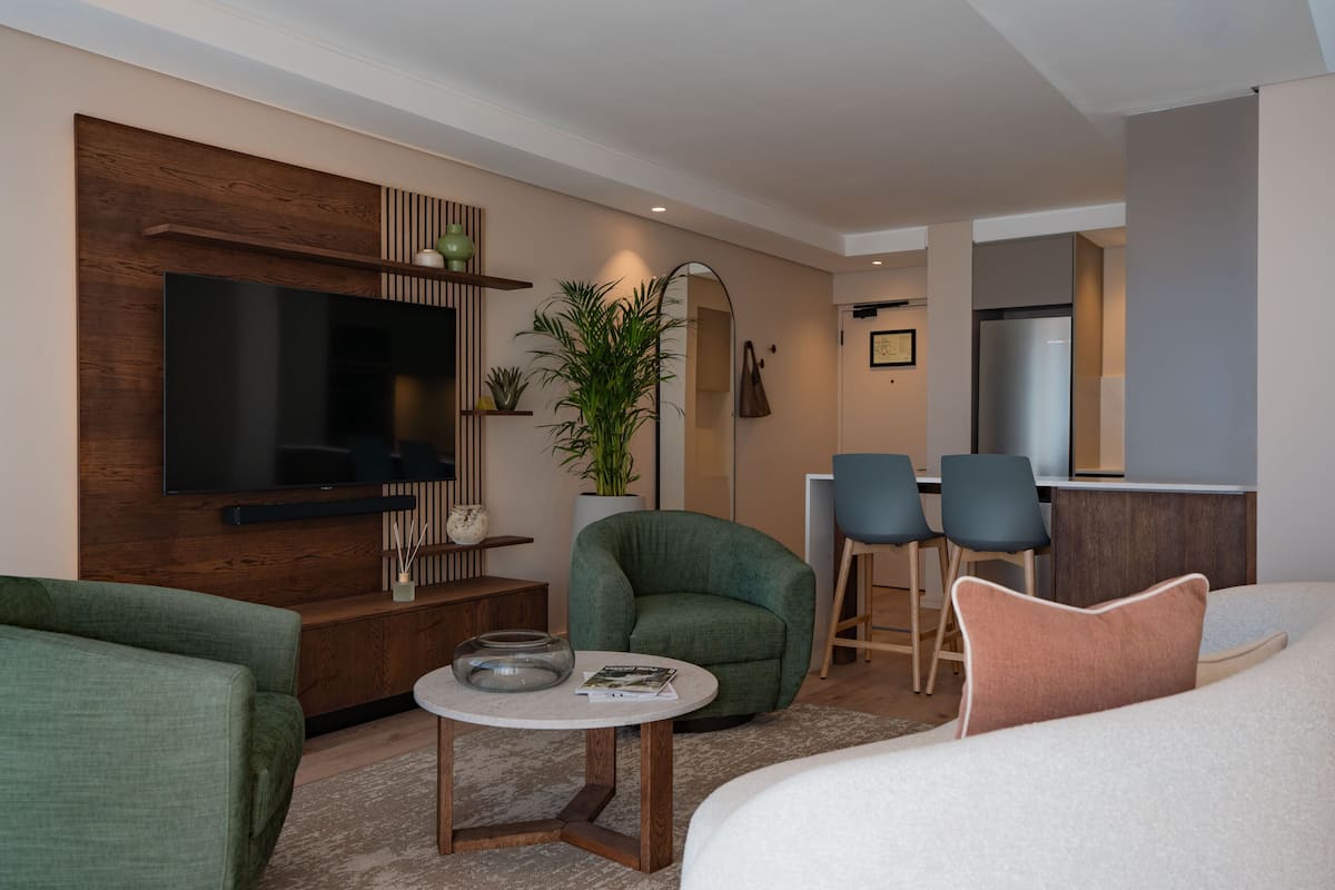 Un salon moderne avec un téléviseur à écran plat, un fauteuil vert, une table basse ronde et un lit agrémenté d’un coussin blanc et pêche.