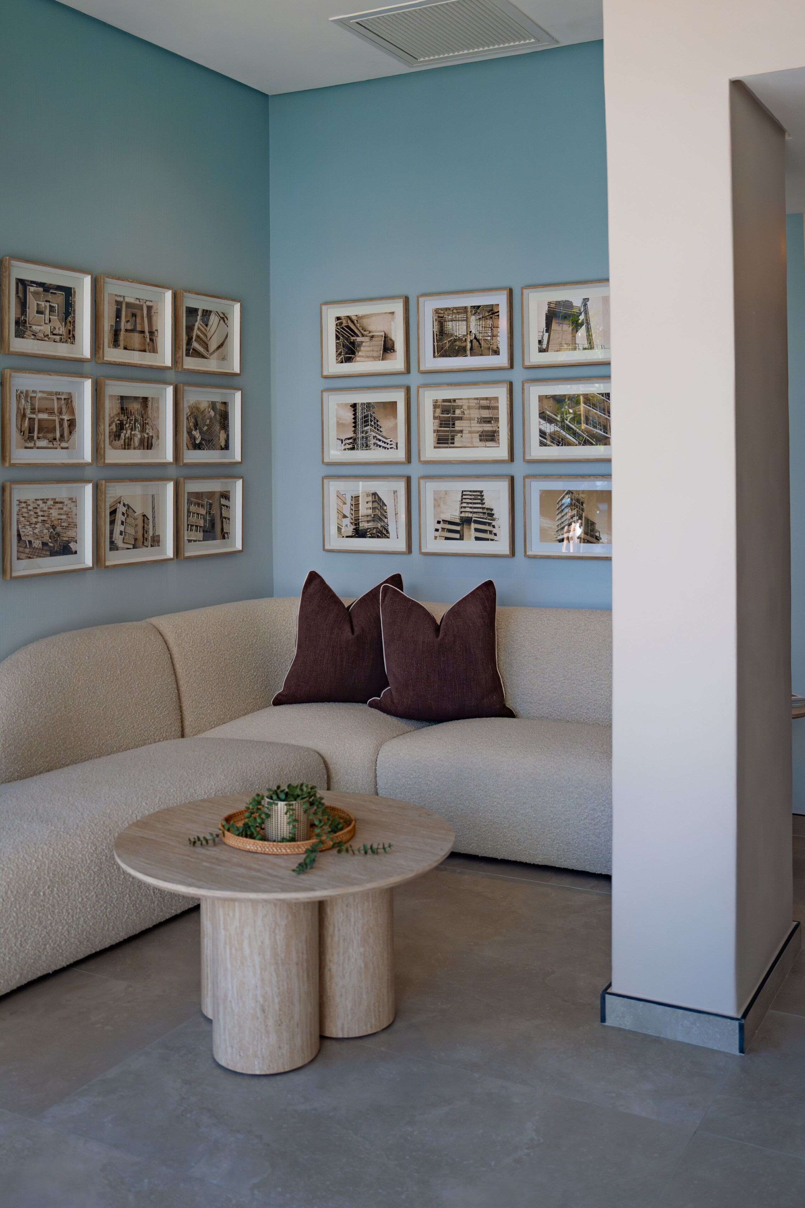 A living room with a beige sofa, a round coffee table with a plant, and framed architectural prints on the wall.