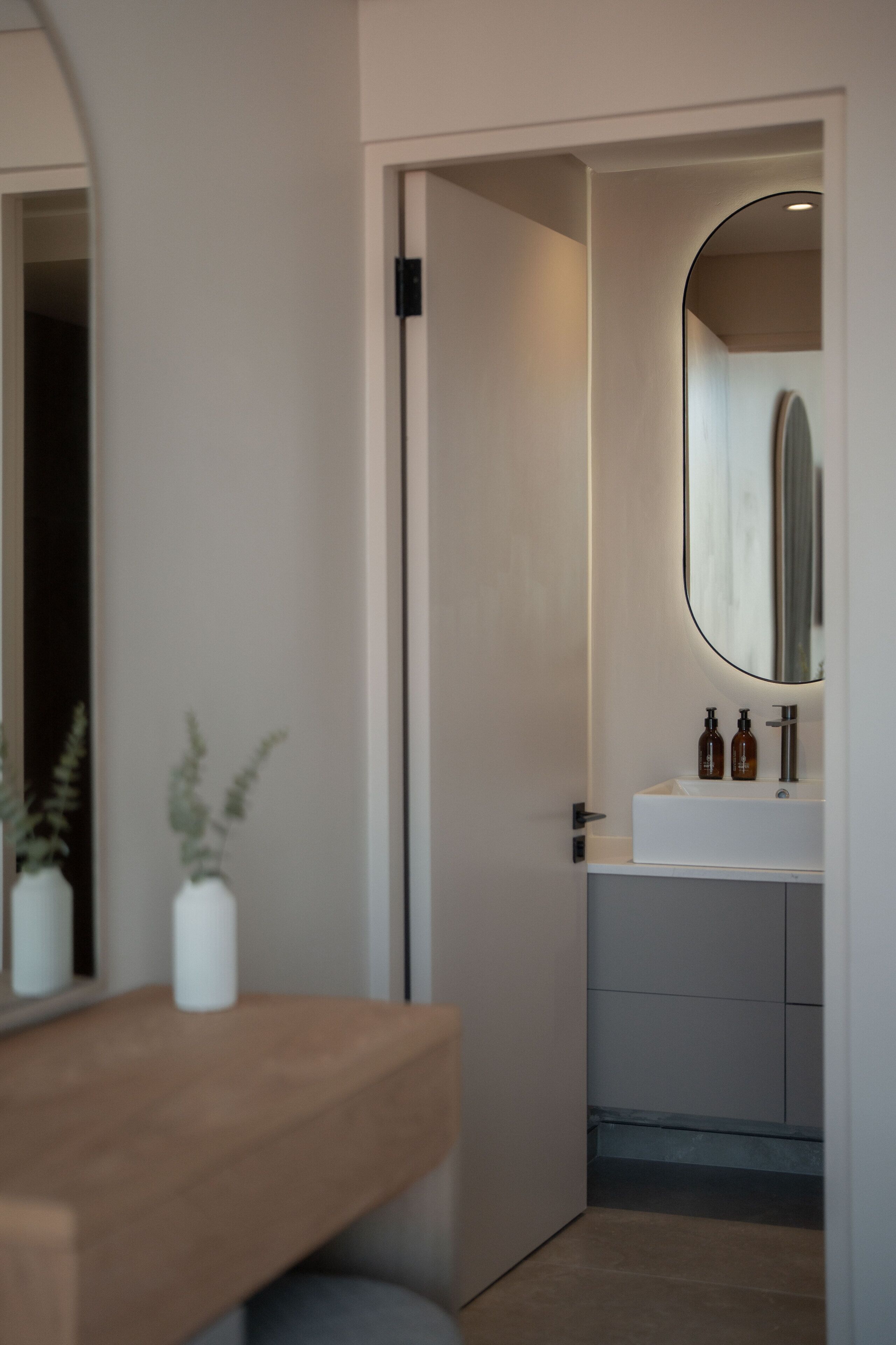 Une salle de bain moderne avec un lavabo blanc, un miroir et deux bouteilles posées sur le comptoir.