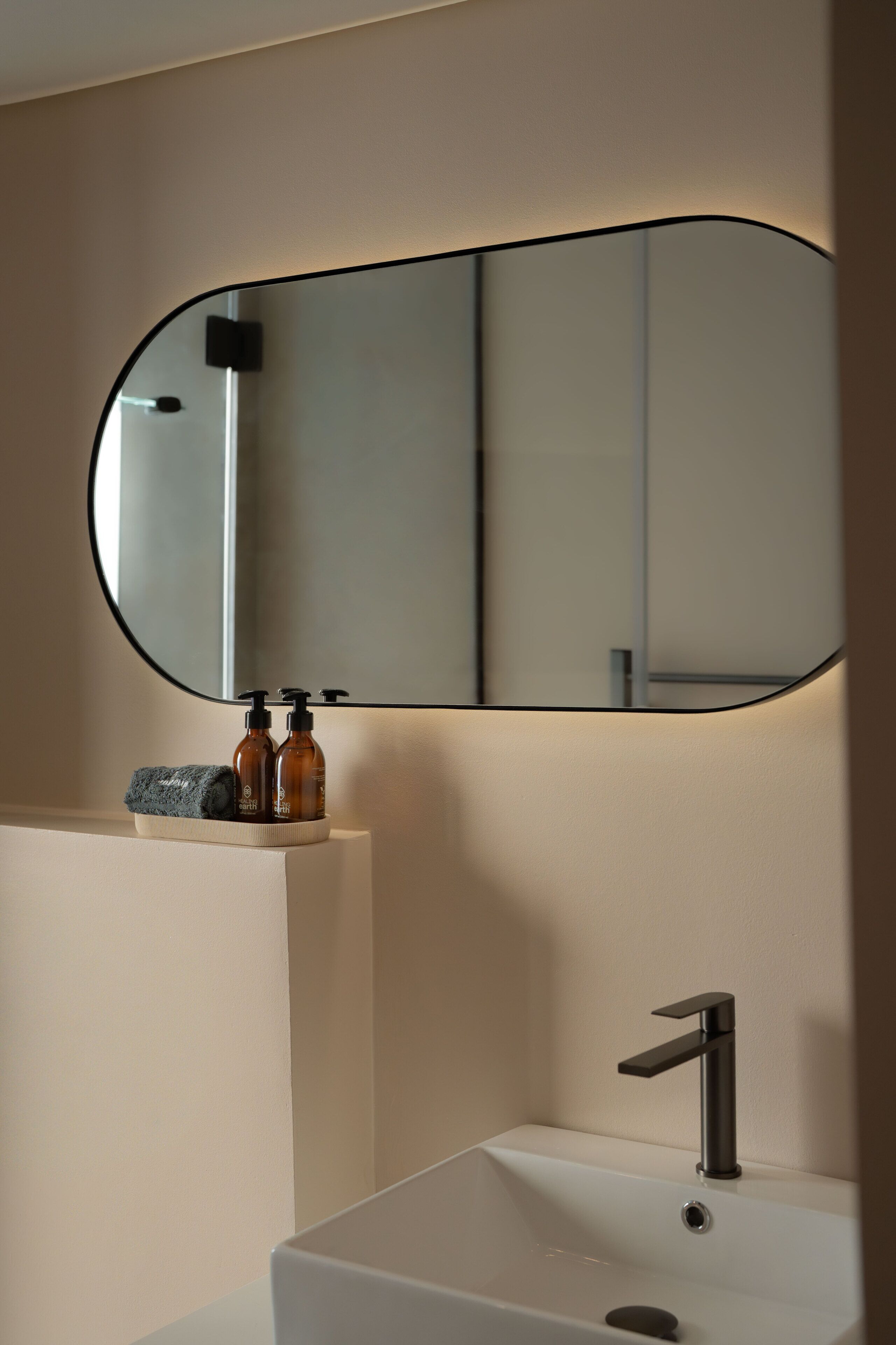 A bathroom with a white sink, a black faucet, a mirror with a black frame, and two brown bottles on the sink.