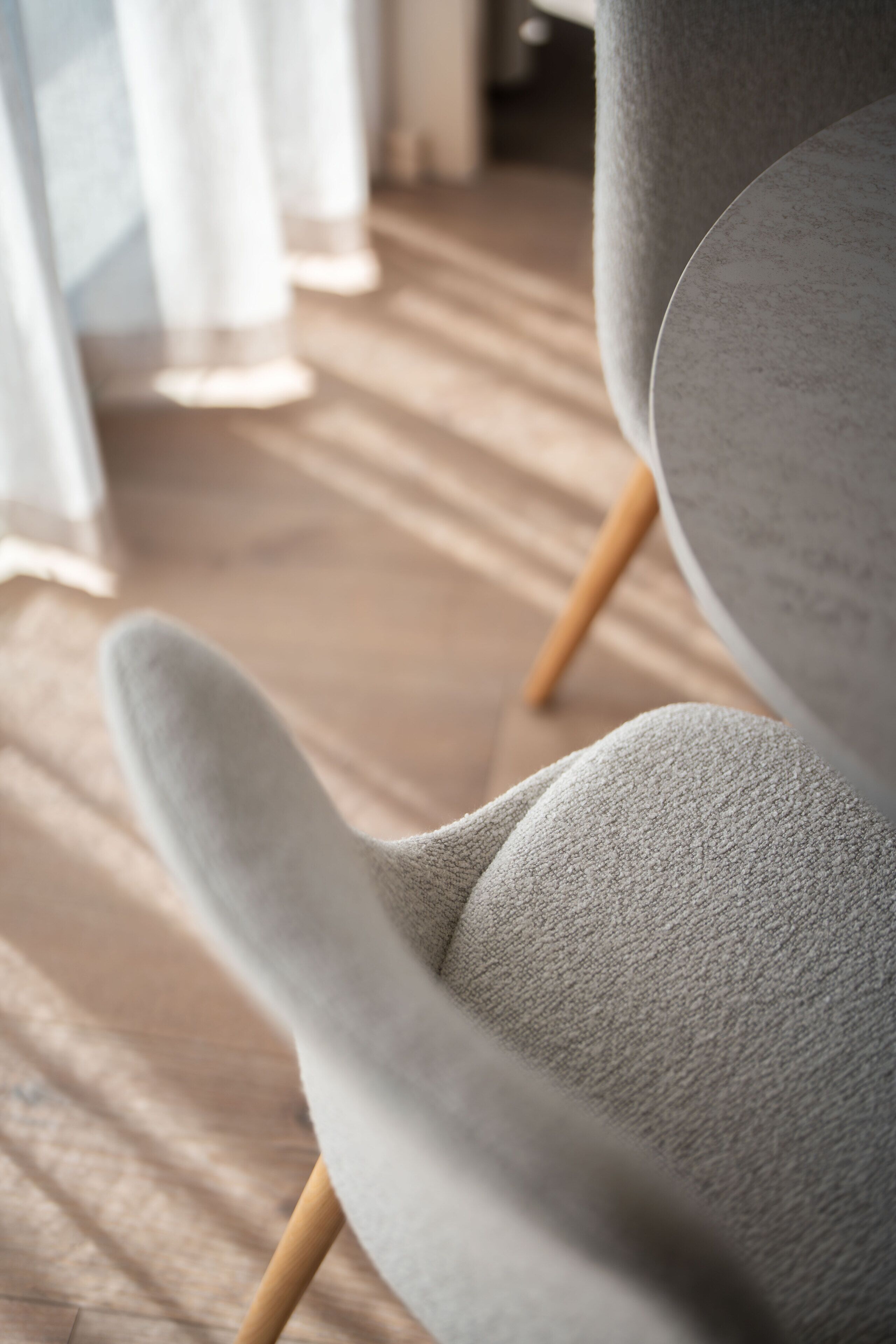 A modern chair with a textured fabric and wooden legs, positioned on a wooden floor.