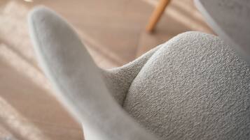 A modern chair with a textured fabric and wooden legs, positioned on a wooden floor.