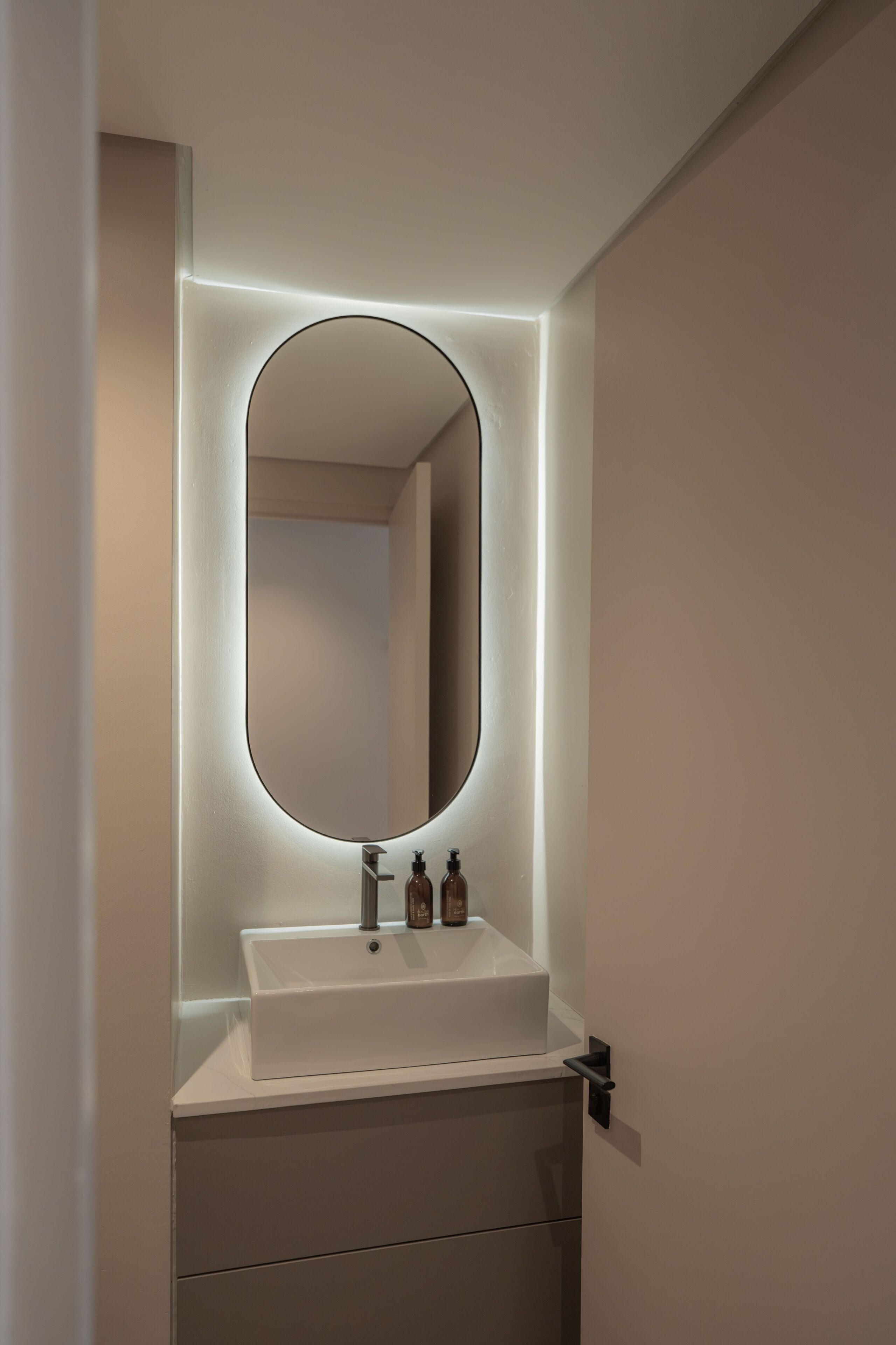Un bagno con un lavandino bianco, uno specchio con cornice illuminata e due flaconi di sapone.