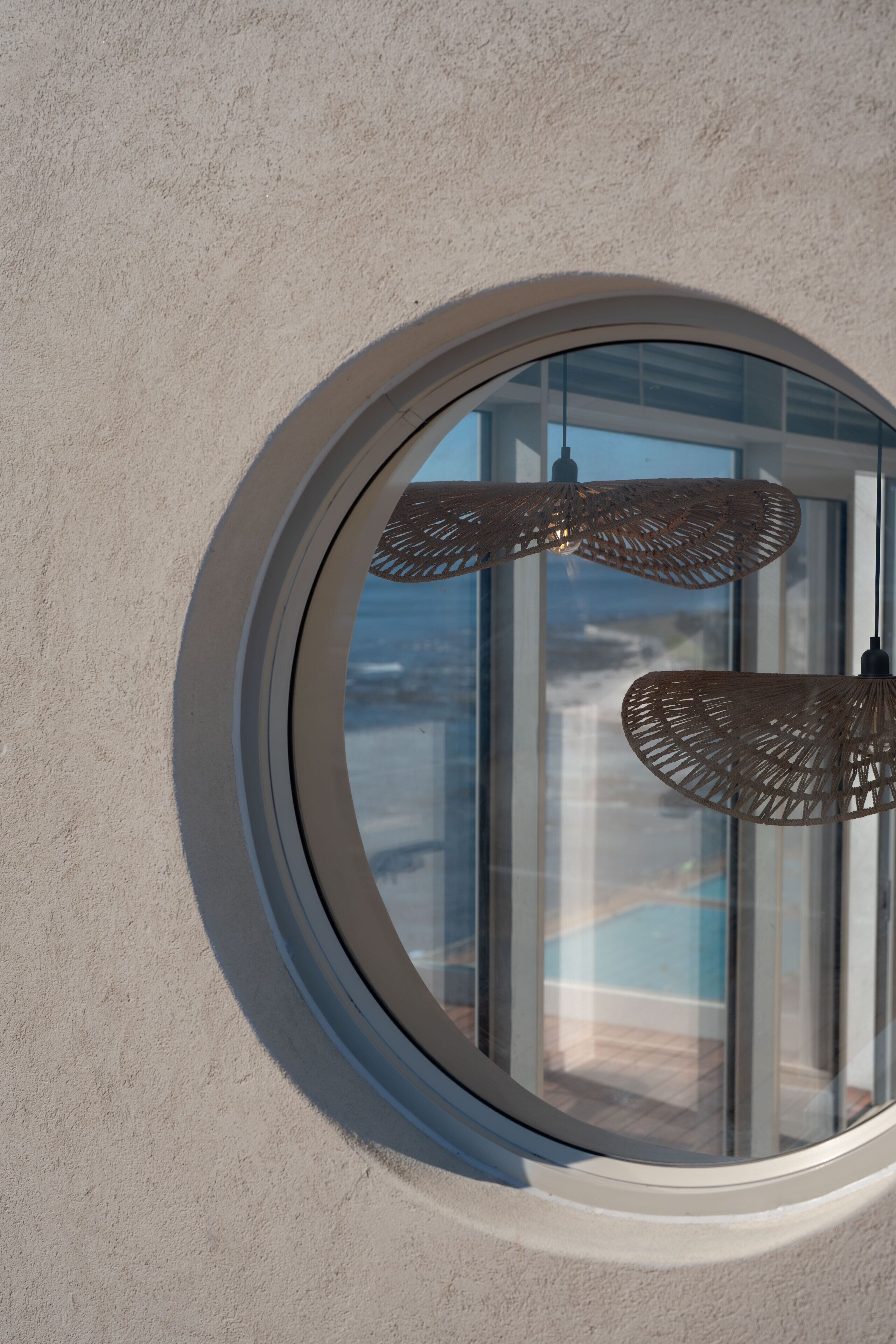 A circular window with a textured wall and two hanging wicker lamps.