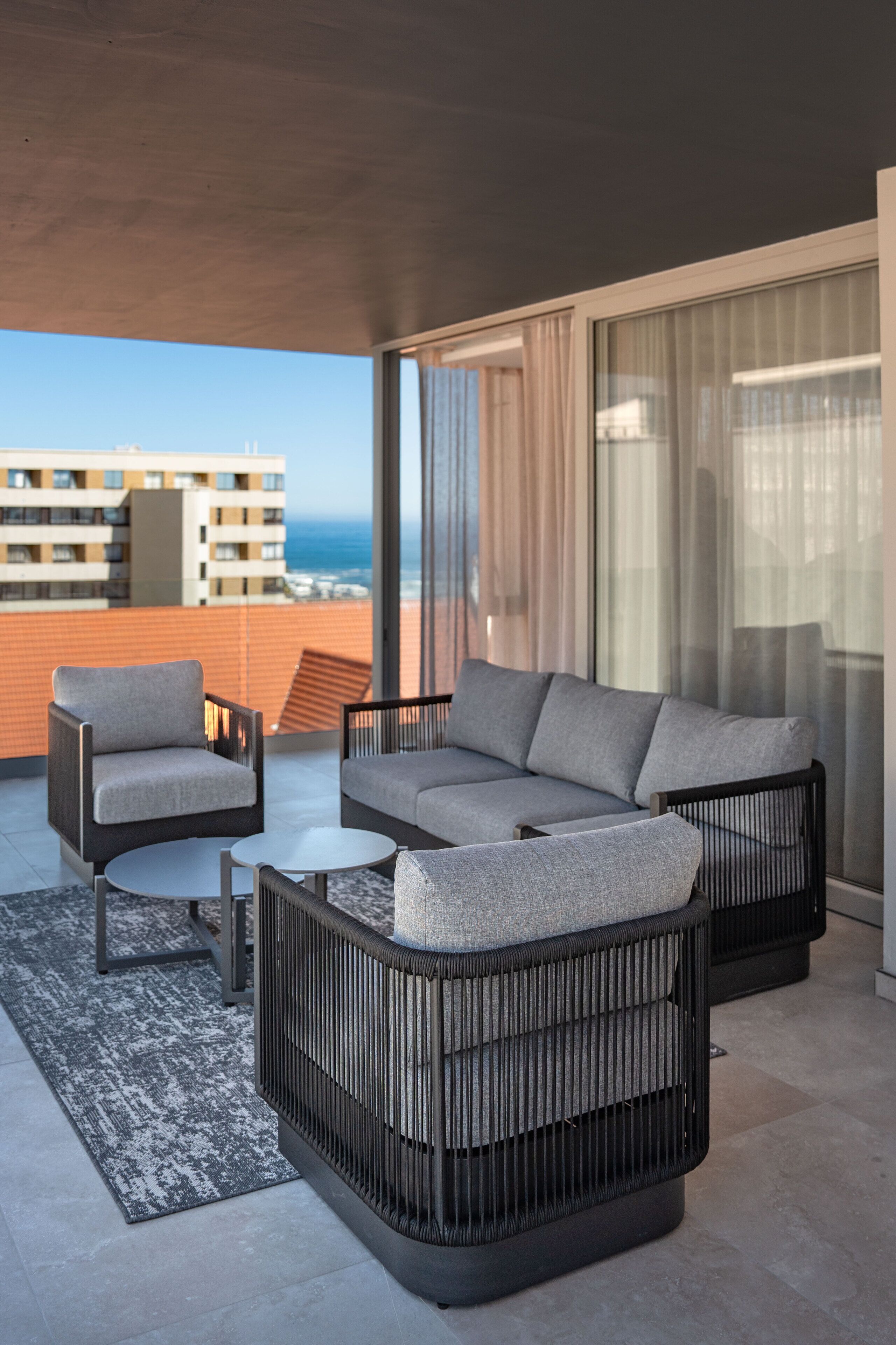Un balcon aménagé avec un canapé, un fauteuil et une table basse, offrant une vue sur le paysage urbain et l’océan.