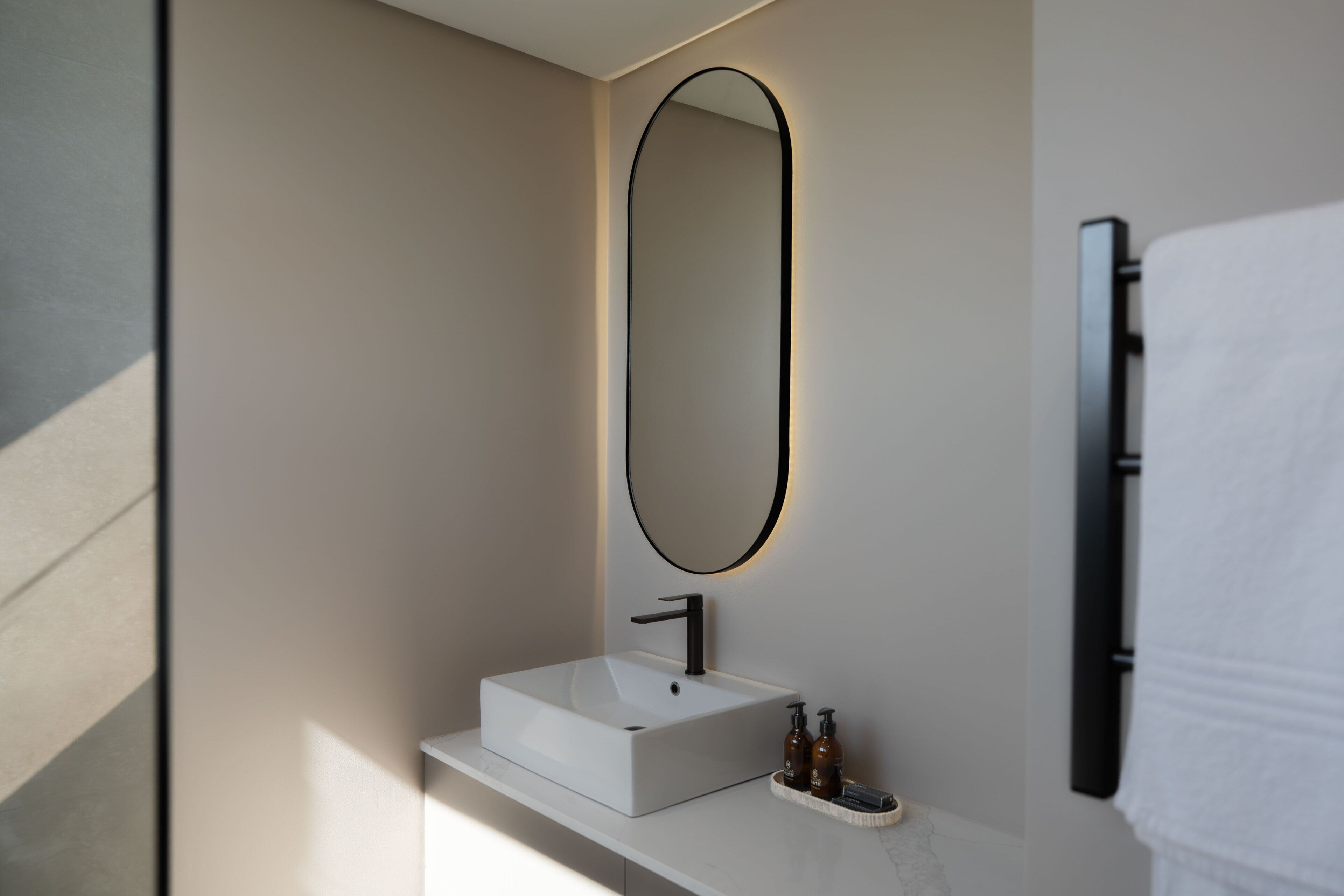 Une salle de bain moderne avec un lavabo blanc, un grand miroir et un porte-serviettes.