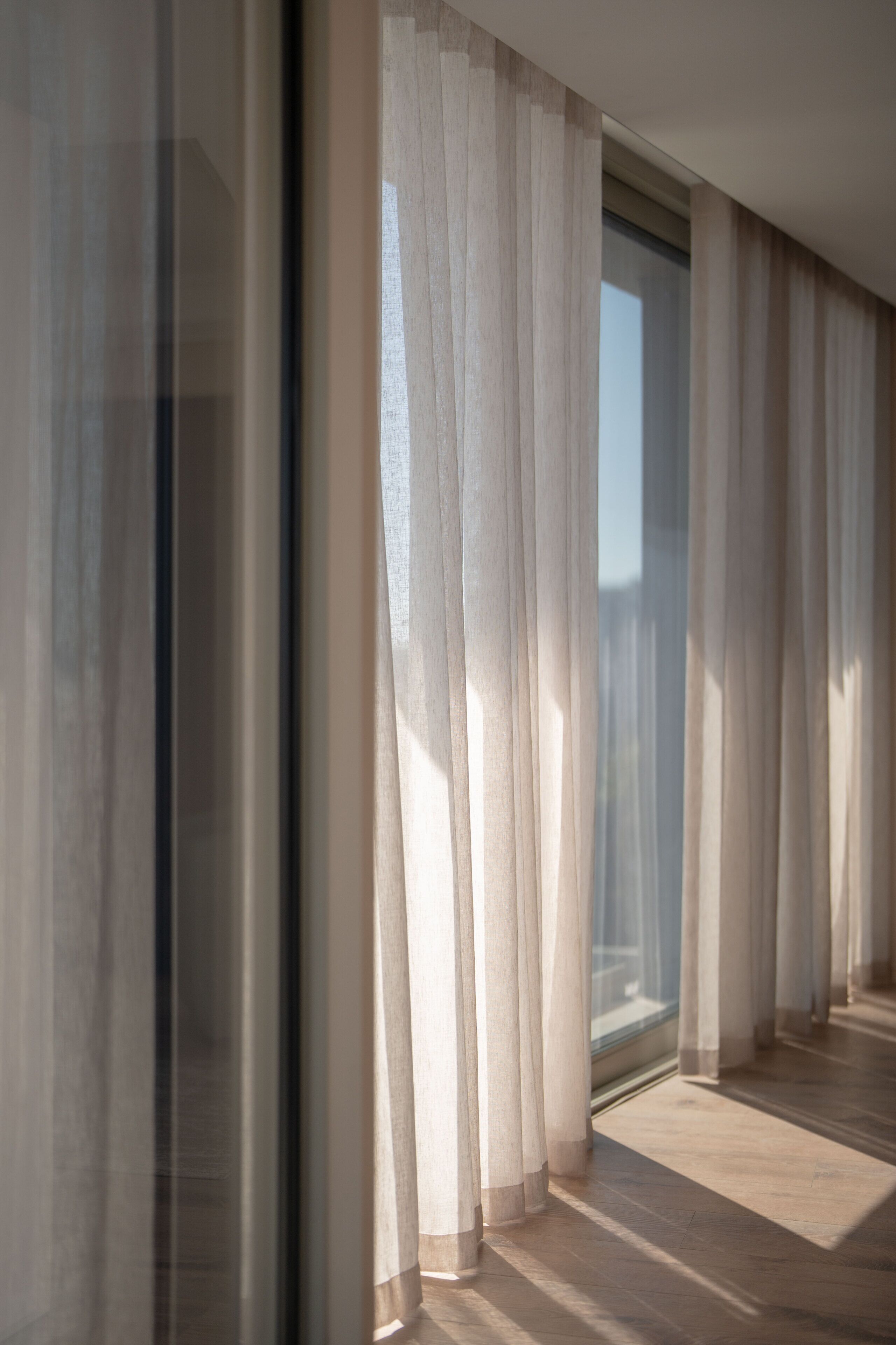 A room with a large window, sheer curtains, and a wooden floor.