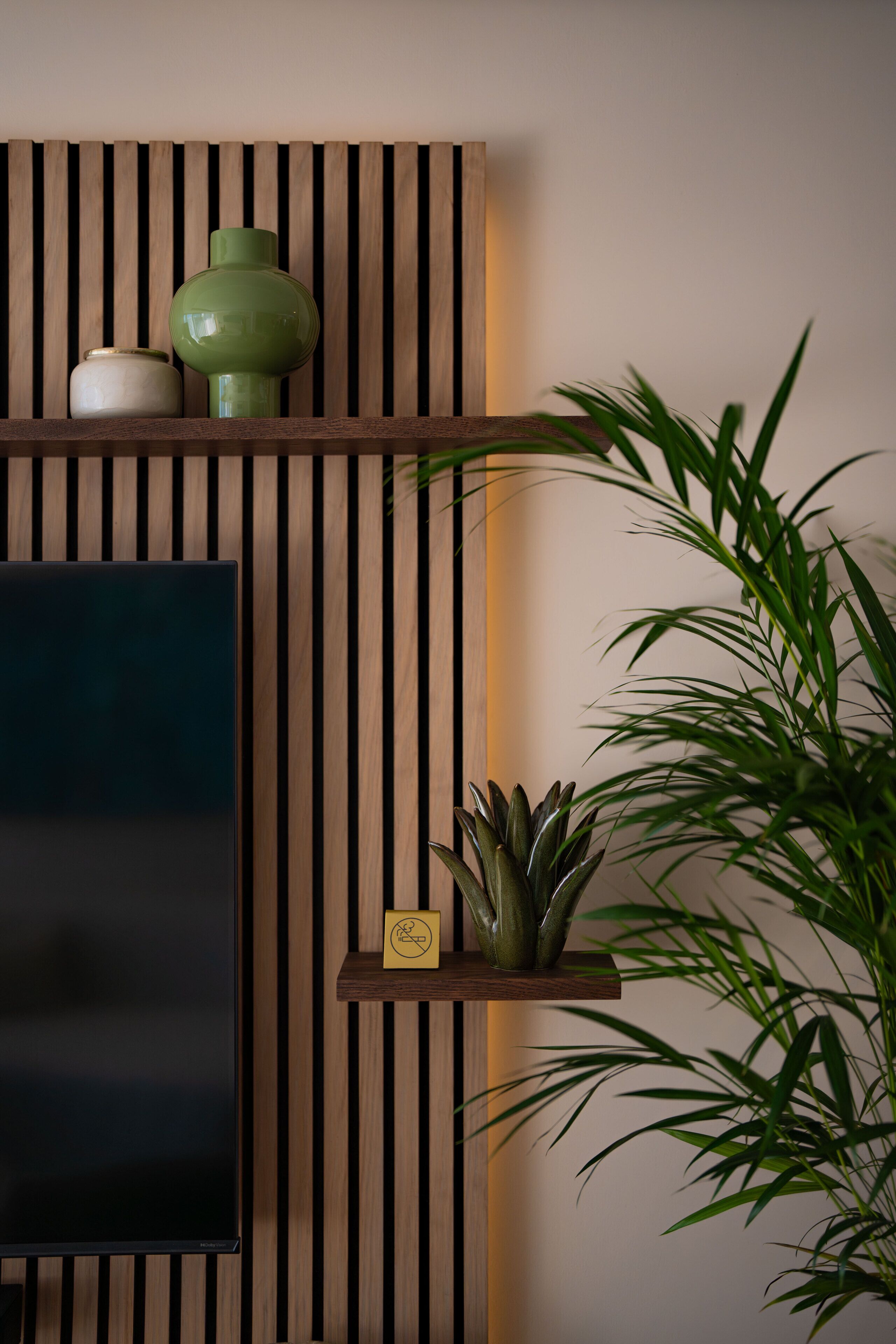 A room with a flat-screen TV, wooden slat wall paneling, a green vase, a small plant, and a bamboo plant.