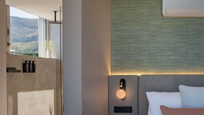 Een moderne hotelkamer met een groot bed, een nachtkastje, een wandairconditioner, een douchegedeelte en uitzicht op het omliggende landschap.