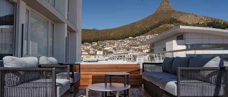 Ein moderner Balkon mit Korbmöbeln, einem kleinen Tisch und Blick auf Berg und Stadt.