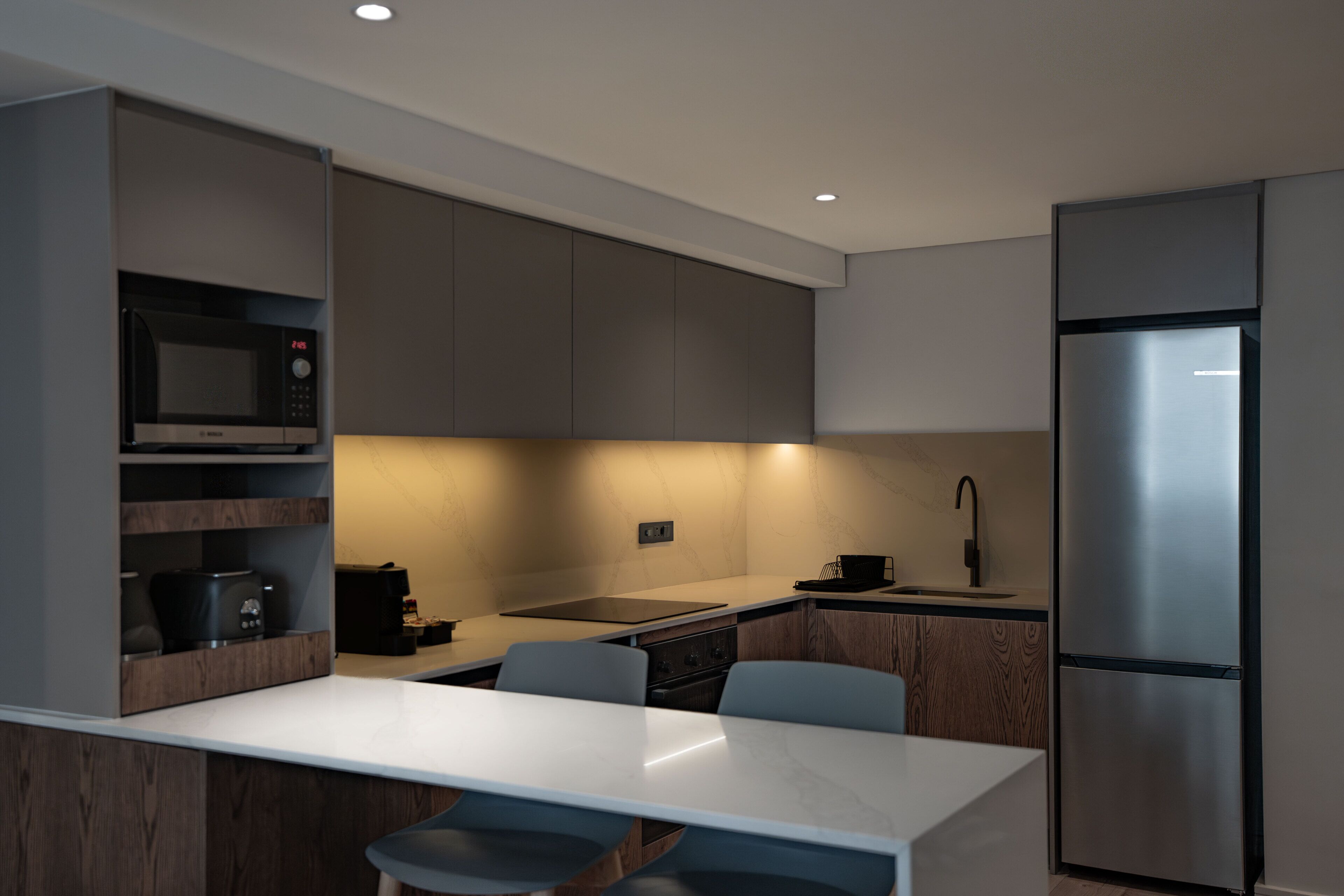 A modern kitchen with a built-in microwave, stove, and sink, a white marble countertop, and a stainless steel refrigerator.