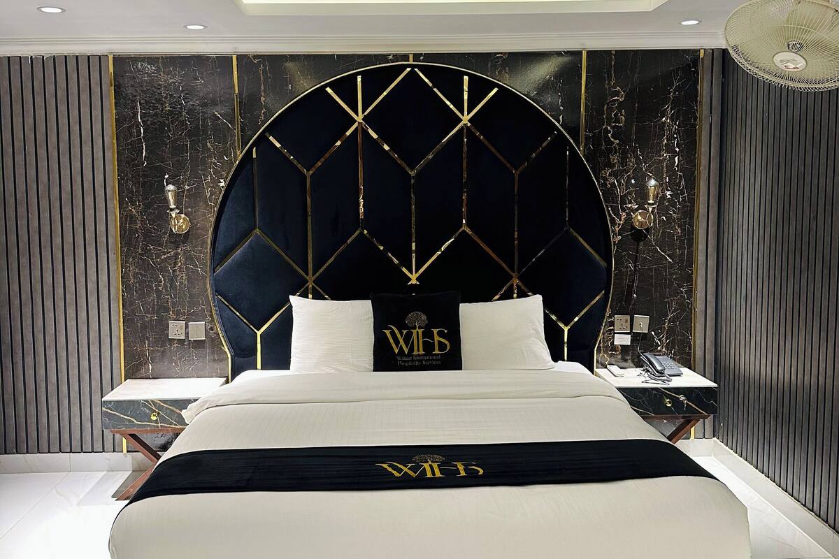 A modern bedroom with a large bed, a decorative headboard, and a nightstand with a lamp.
