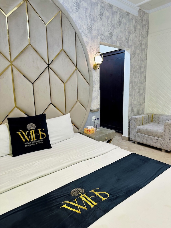 A hotel room with a large bed, a headboard with a geometric pattern, a black and gold pillow, a nightstand, a sofa, and a patterned wall. - Walnut Hotel Islamabad (Islamabad)