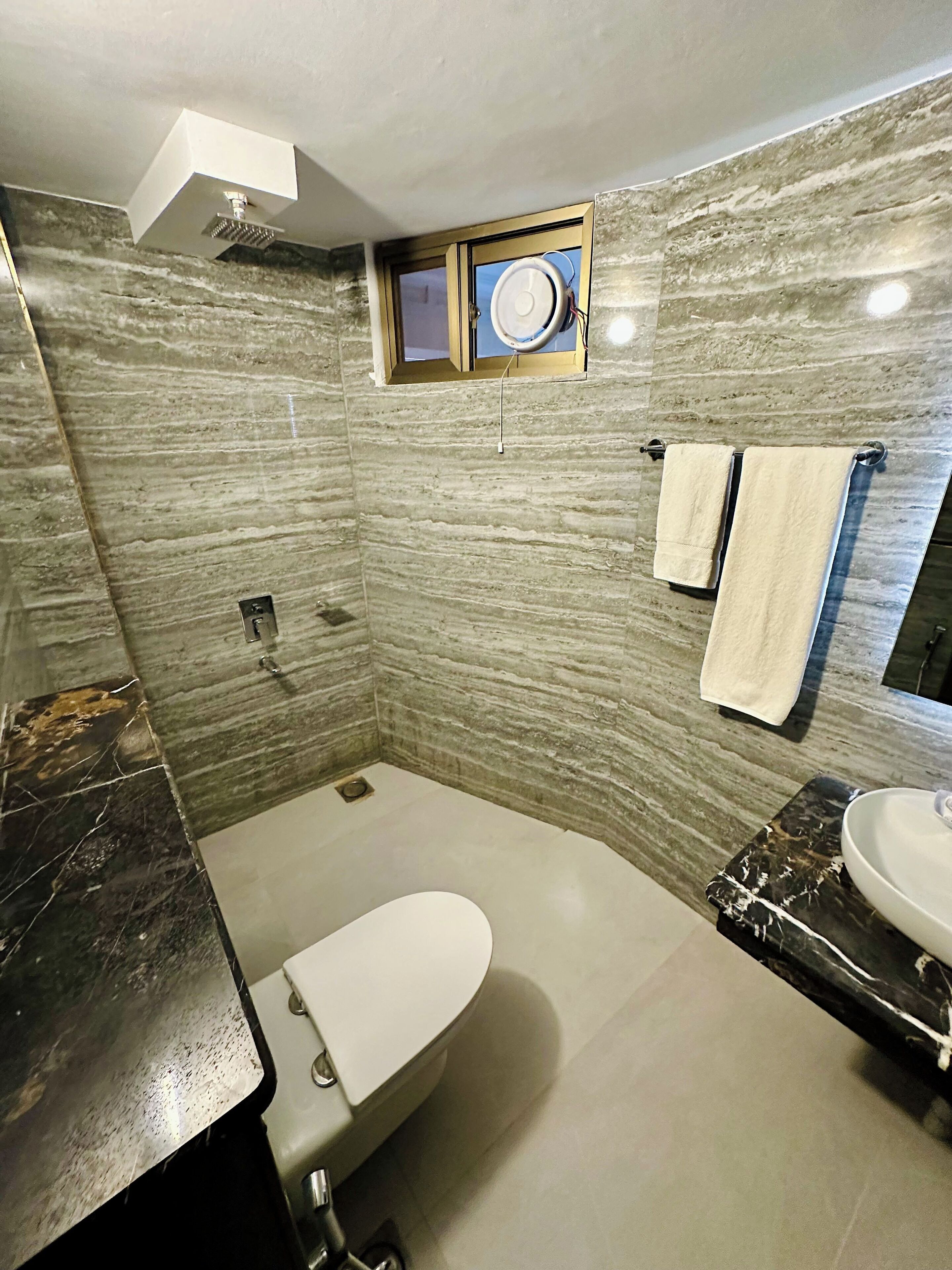 Et badeværelse med marmorvæg, toilet, håndvask og et håndklædetørrestativ.