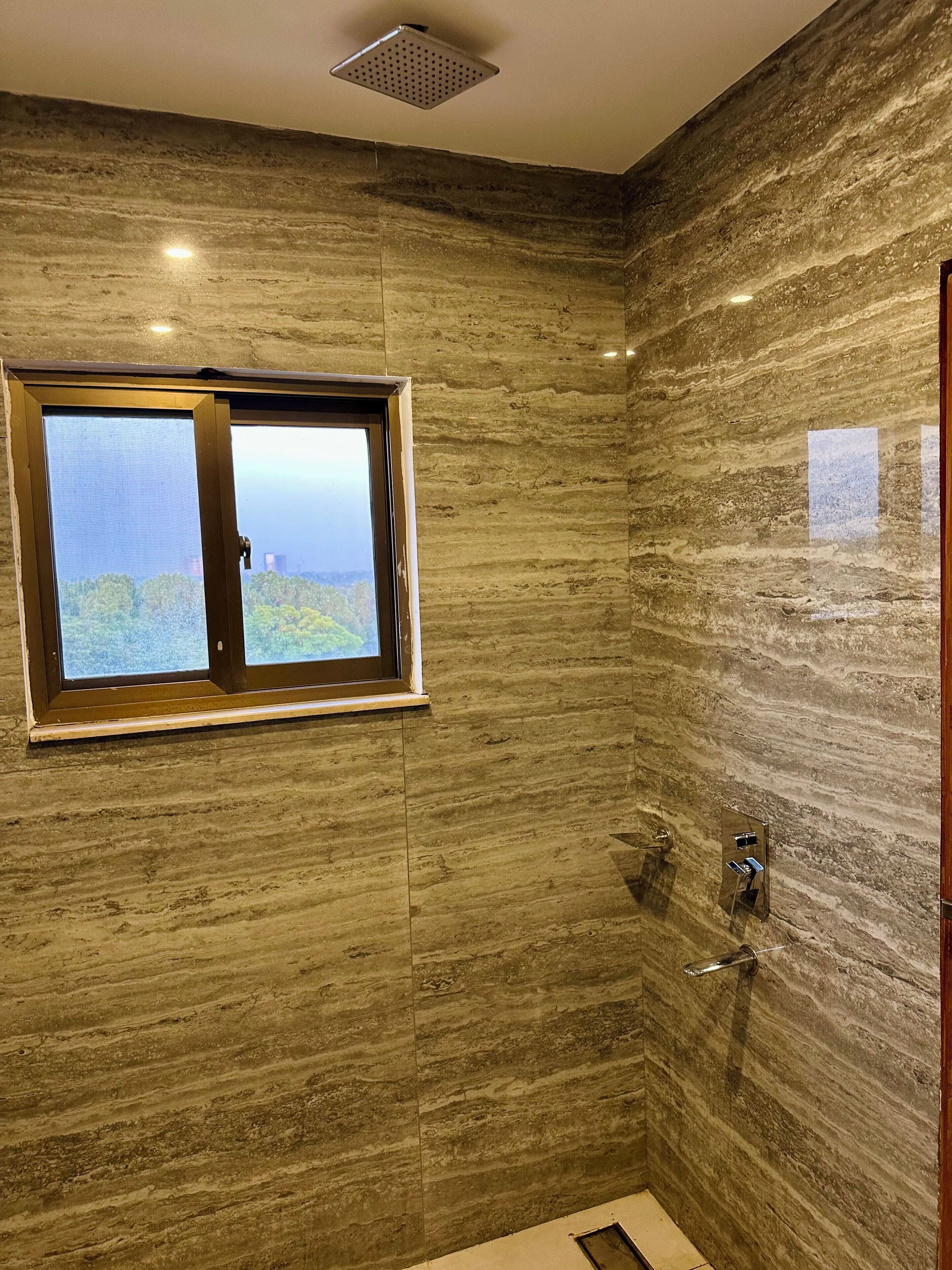 A bathroom with a large window, marble walls, and a shower area.