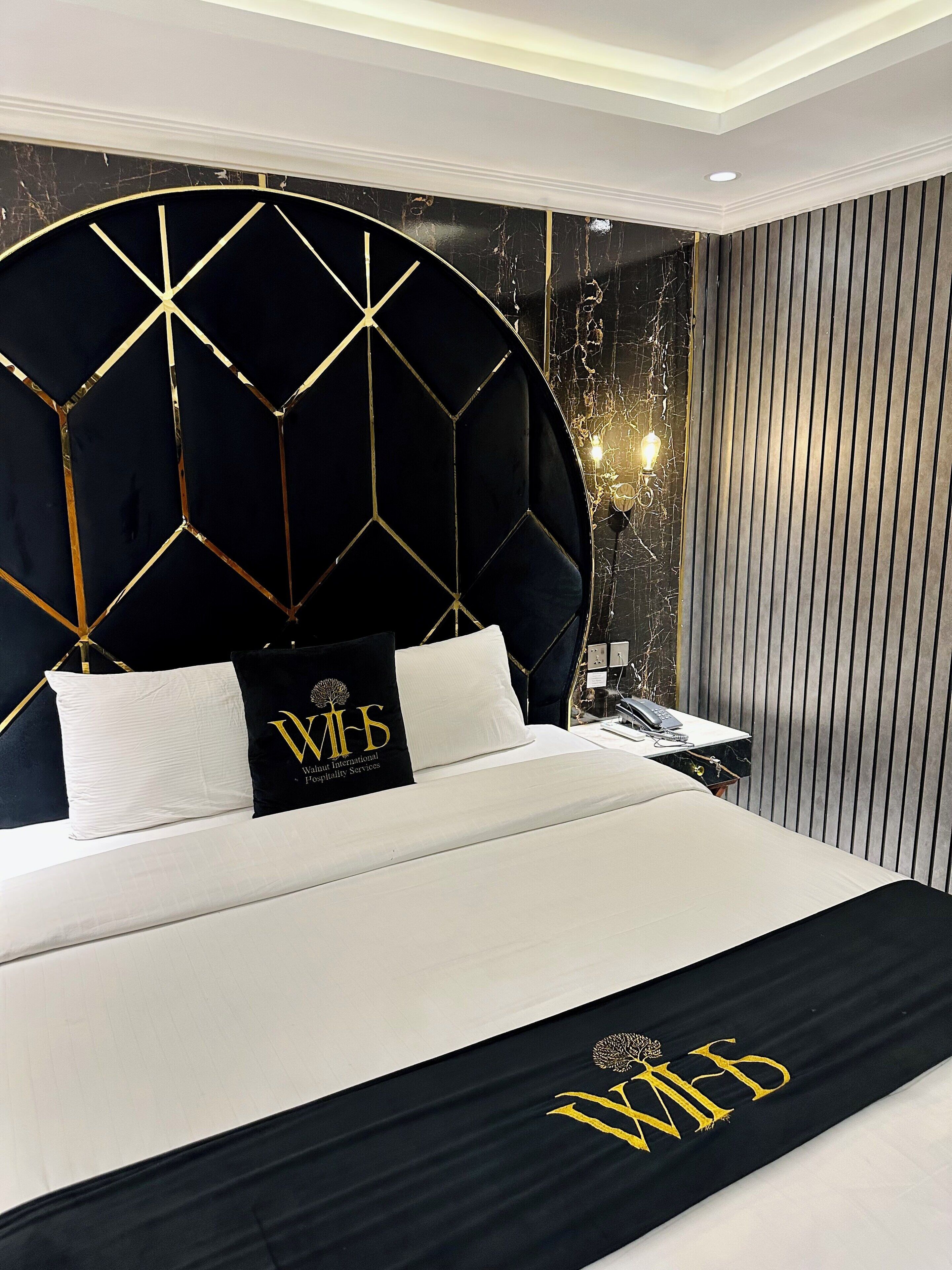 A hotel room with a large bed, a decorative headboard, and a nightstand with a lamp.