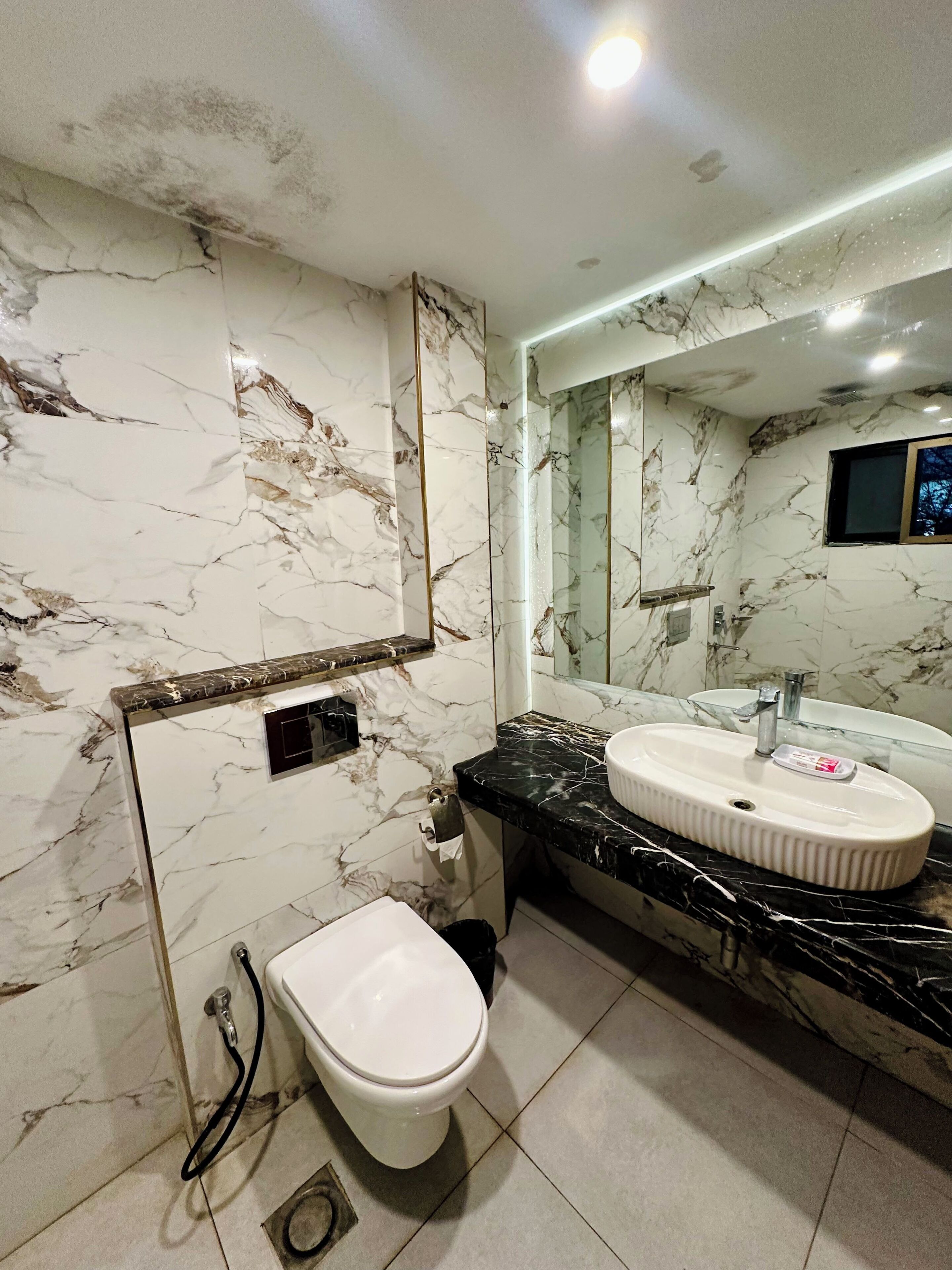 A modern bathroom with marble walls, a black countertop, a white sink, and a toilet.