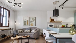 A modern kitchen with a grey sofa, dining table, and chairs. There are two wall-mounted light fixtures and a hanging pendant light.