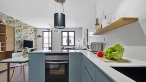A modern kitchen with a central island, built-in oven, and a wooden shelf above the counter.