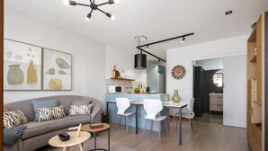 A modern living room with a sofa, coffee table, and dining area. There is a kitchen in the background with a microwave, sink, and cabinets.