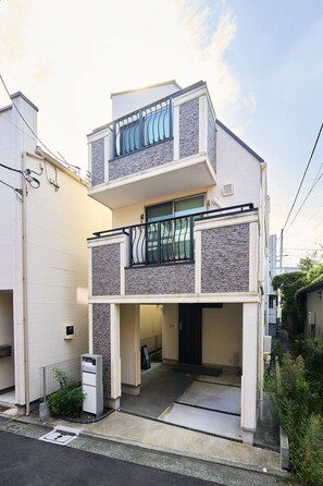 A two-story residential building with a balcony, a garage entrance, and a small garden area.