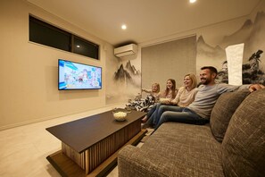Een woonkamer met een flatscreen televisie, een houten salontafel en een bank.