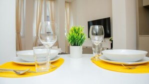Et spisebord dækket med hvide tallerkener, klare glas og en lille potteplante.