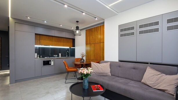 A modern living room with a grey sofa, a round coffee table, and a dining area with a wooden table and orange chairs. - Apartment by Luxe Group KO333 (Yerevan)
