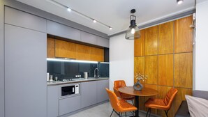 A modern kitchen with grey cabinets, a wooden accent wall, and a dining area with orange chairs. - Apartment by Luxe Group KO333 (Yerevan)