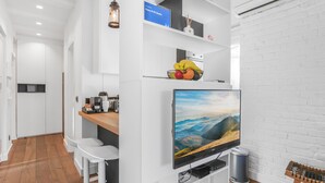 Ein modernes Wohnzimmer mit Flachbildfernseher, weißen Einbauschränken, einem Holzesstisch und einer Ziegelwand.