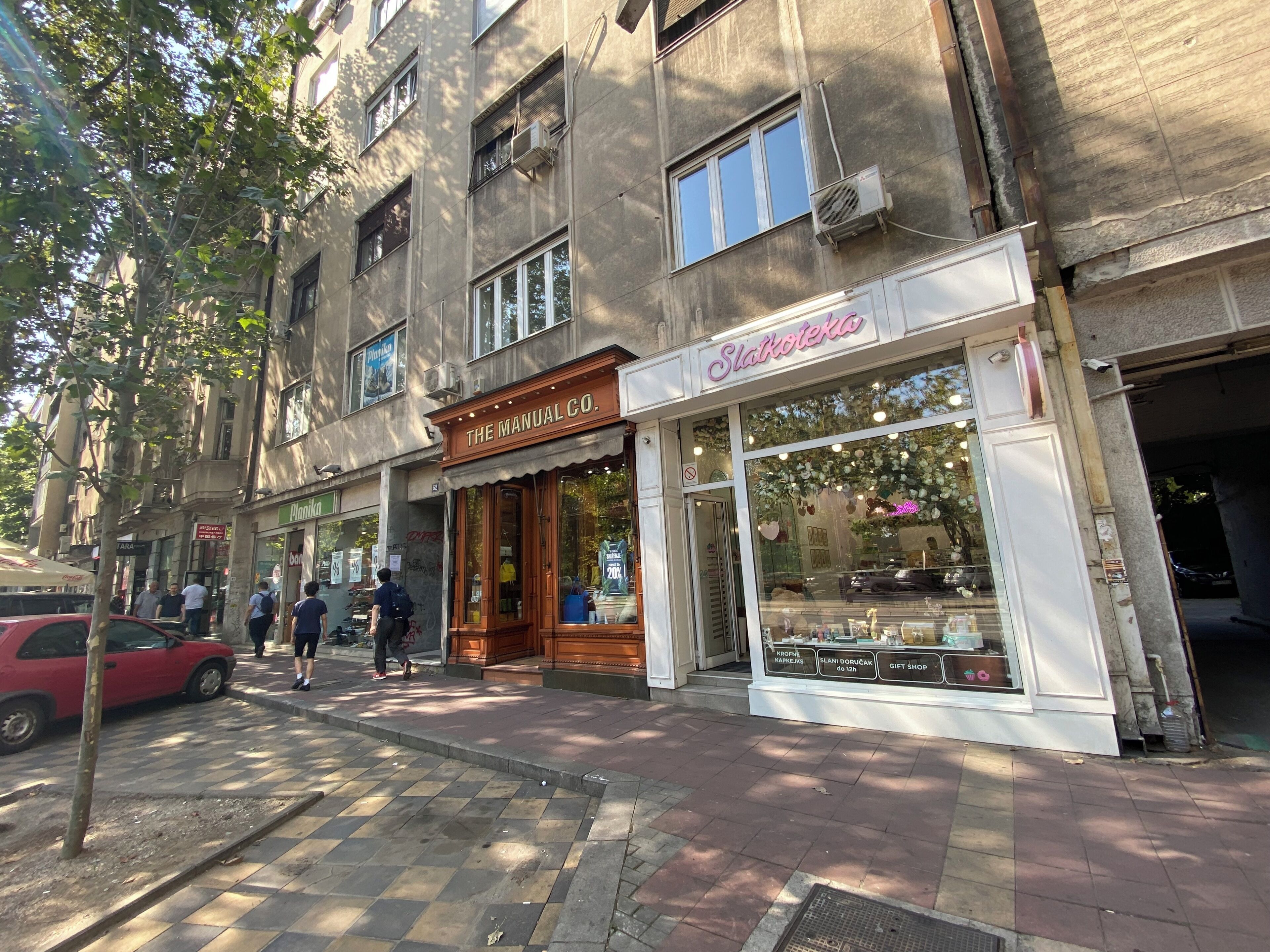 Une vue de rue d’un immeuble abritant un magasin appelé « Slatkotekija », avec une façade en verre et une enseigne.