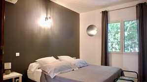 A bedroom with a bed, bedside table, lamp, and a window with curtains. - Mas de Cerier (Saint-Gilles)