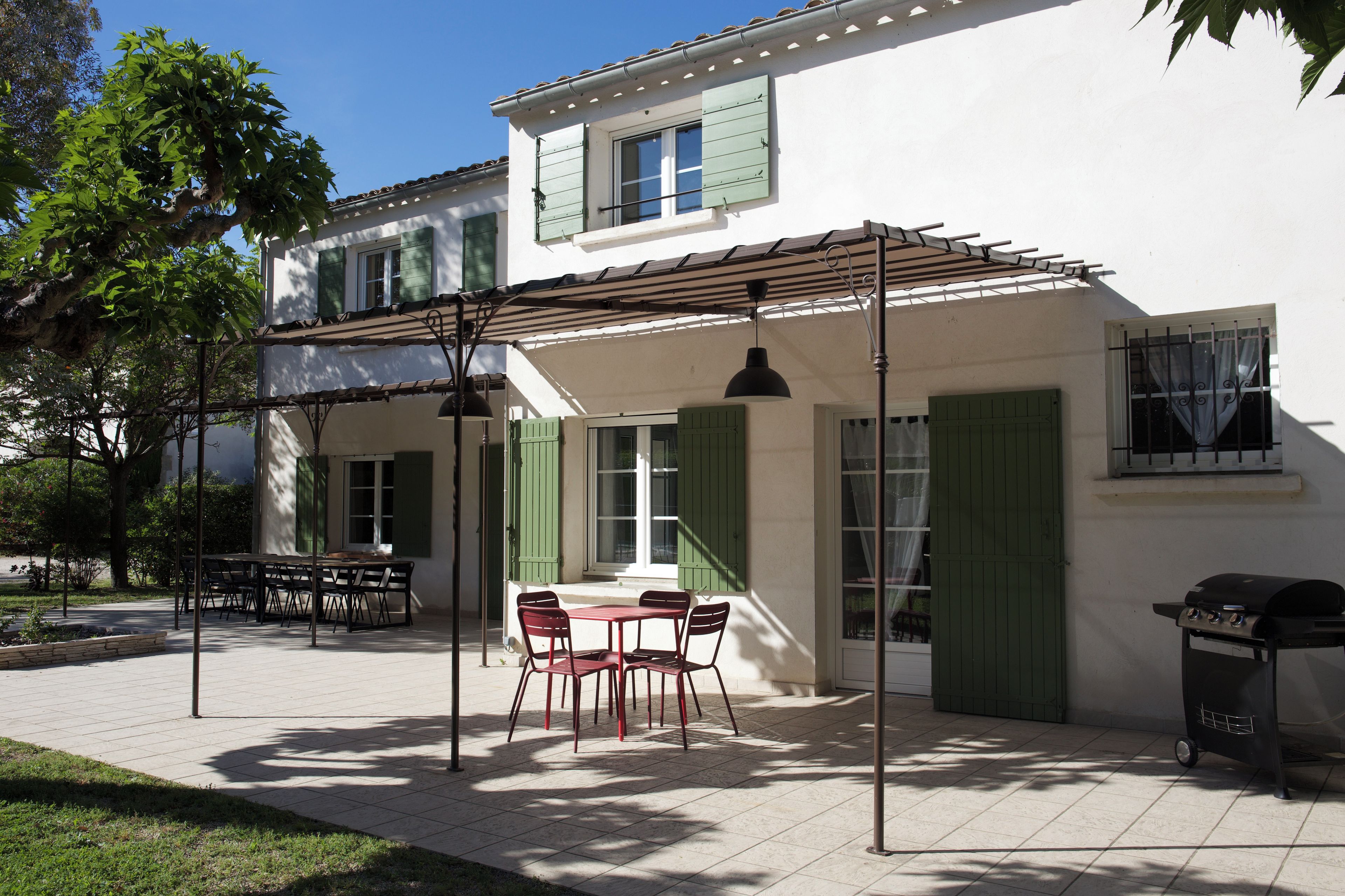 A patio with a table and chairs, a grill, and a pergola with hanging lights.