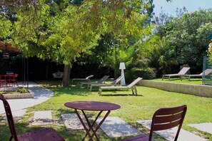 A patio area with a table and chairs, surrounded by a garden with trees and a lawn. - Mas de Cerier (Saint-Gilles)