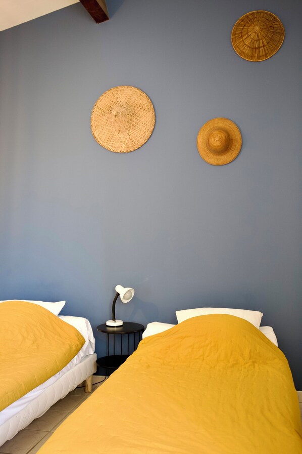 A bedroom with two beds, a nightstand, and two woven hats on the wall.