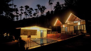 A modern house with a swimming pool, surrounded by a fence, and palm trees in the background. - Prakrithi Luxe Retreat (Vythiri)