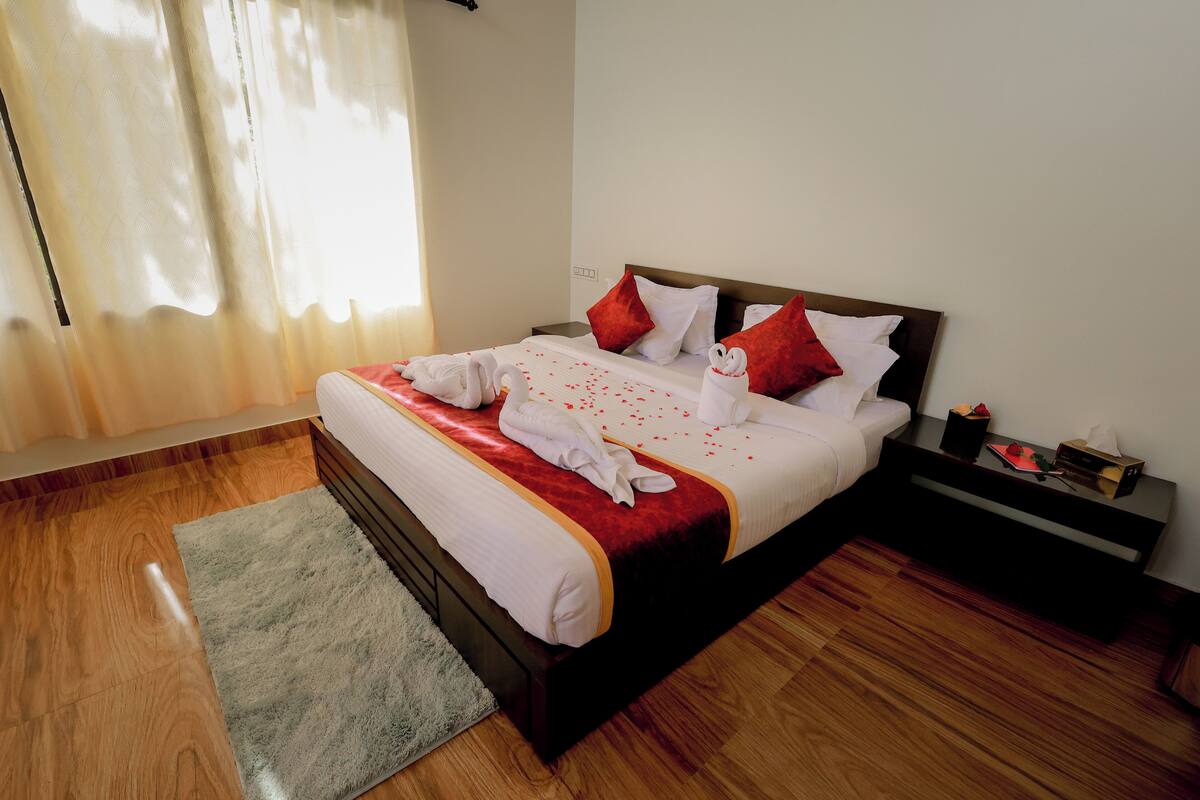 A neatly made bed with white and red bedding, a wooden floor, and a small bedside table with a lamp.