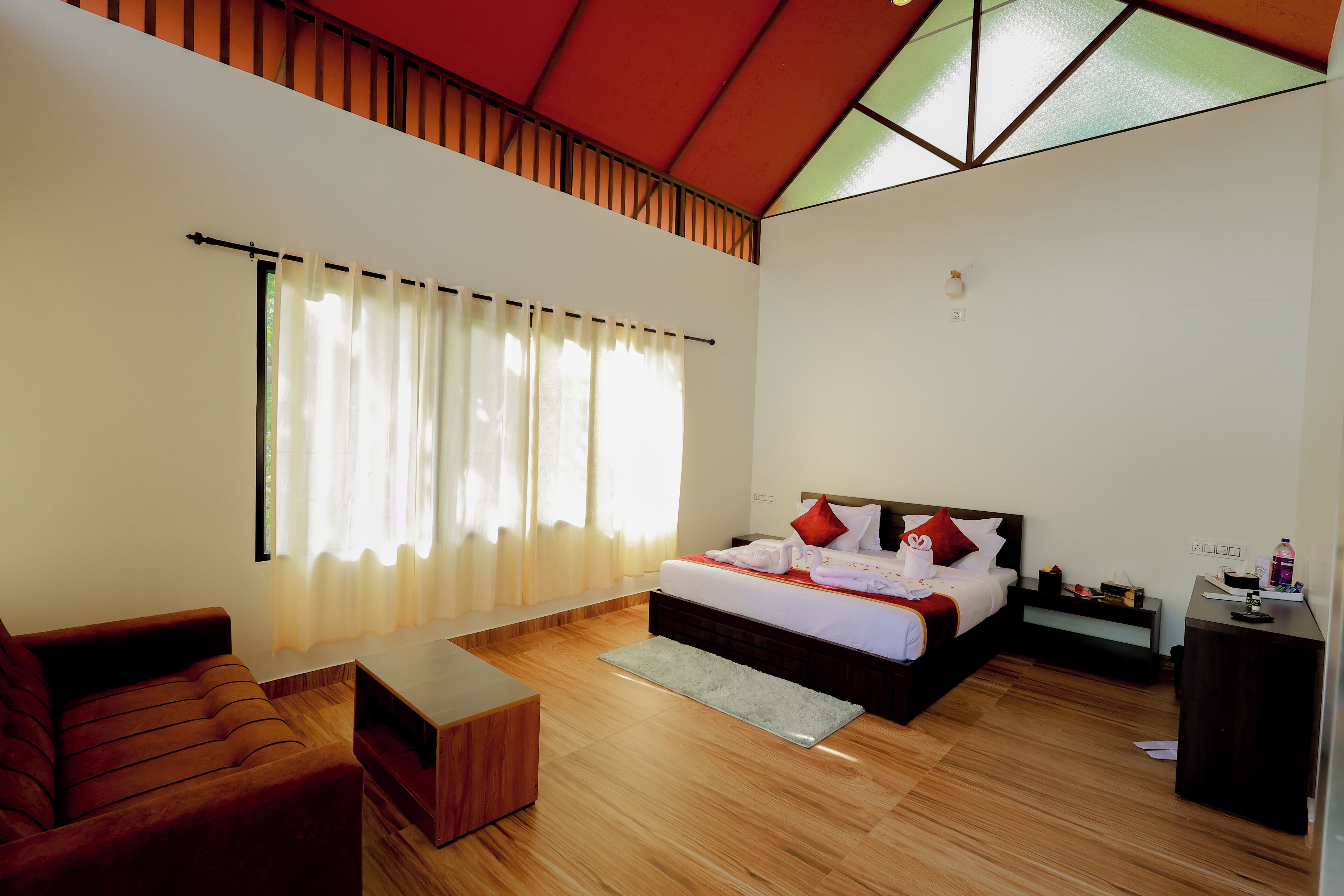 A modern hotel room with a bed, a sofa, a desk, and a large window with curtains.