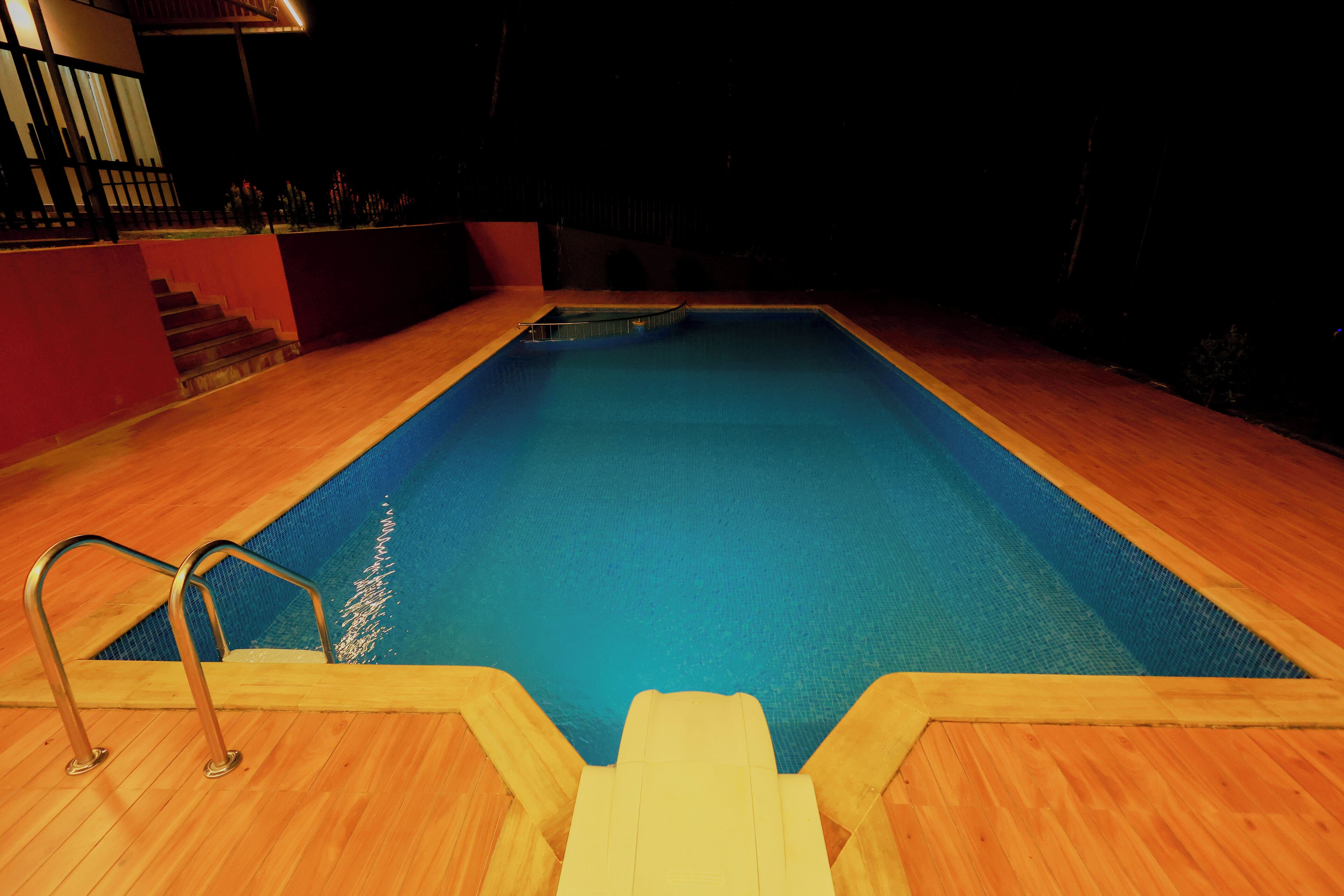 A swimming pool with a wooden deck and metal handrails.