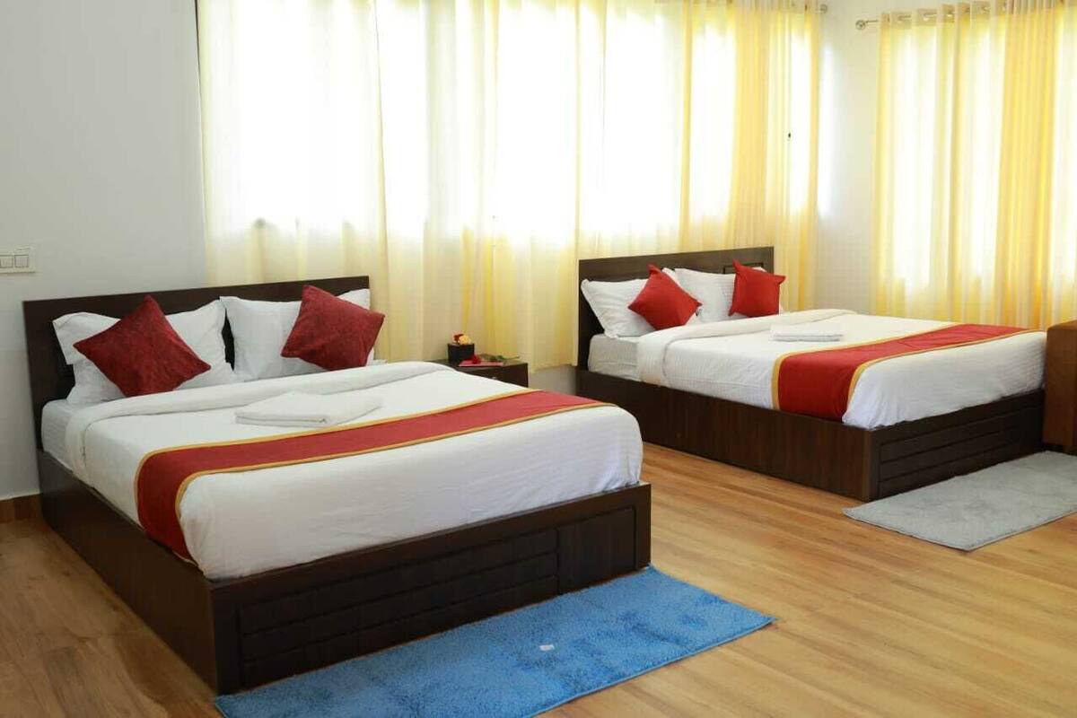 A hotel room with two beds, each with white bedding and red accents, wooden headboards, and a blue rug.