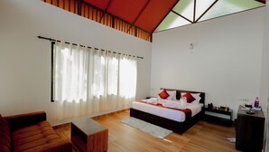 A modern hotel room with a large bed, a sofa, a desk, and a window with curtains. - Prakrithi Luxe Retreat (Vythiri)