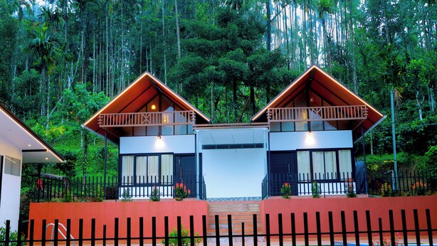 A two-story building with a balcony, surrounded by a pool and a fence. - Prakrithi Luxe Retreat (Vythiri)