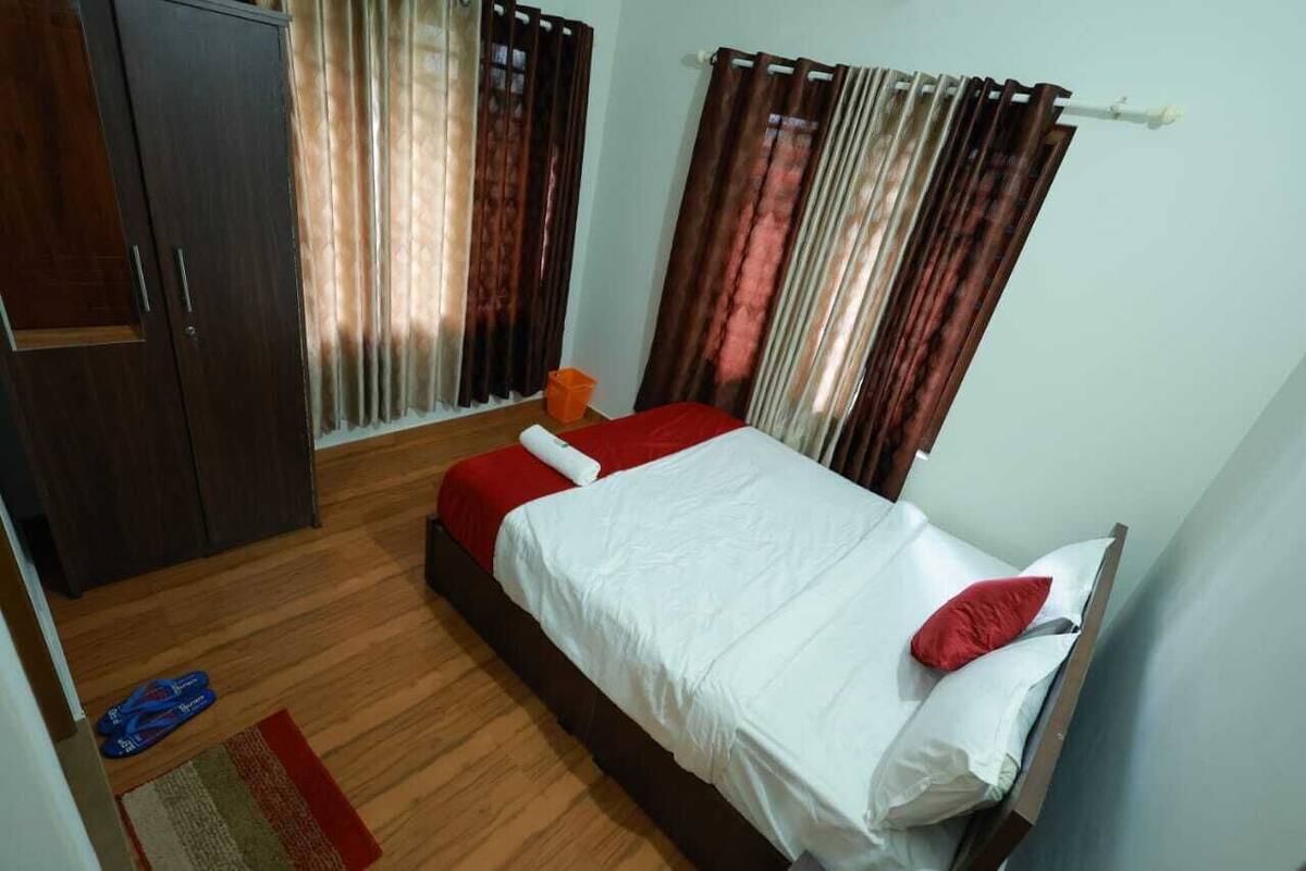 A bedroom with a bed, wooden wardrobe, curtains, and a small rug.