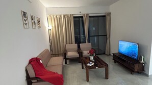 Una sala de estar con sofá, dos sillones, una mesita de centro, televisor y ventilador de techo.