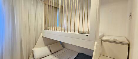 A bunk bed with a pull-up ladder, a bedside table, and a small cabinet.