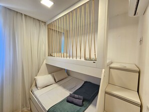 Una cama litera con escalera y una mesita de noche, junto con un mueble pequeño.